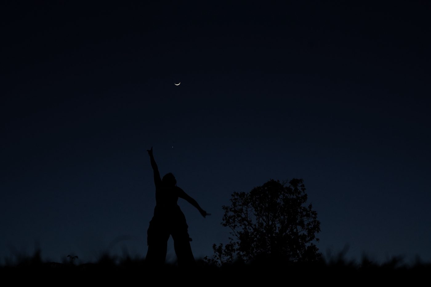 Silhouette reaching for the crescent moon at dusk